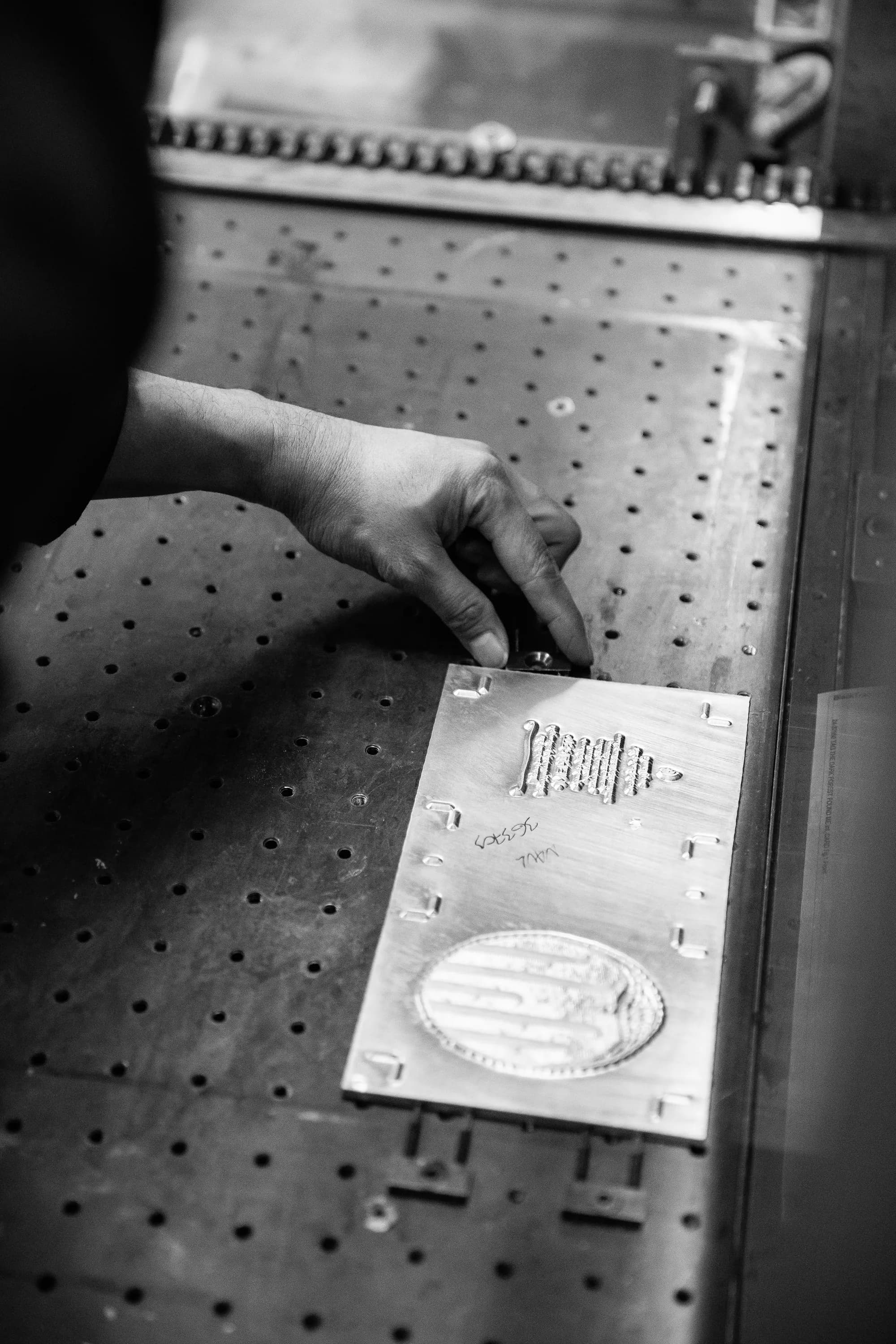 A hand setting a metal printing plate on a press bed