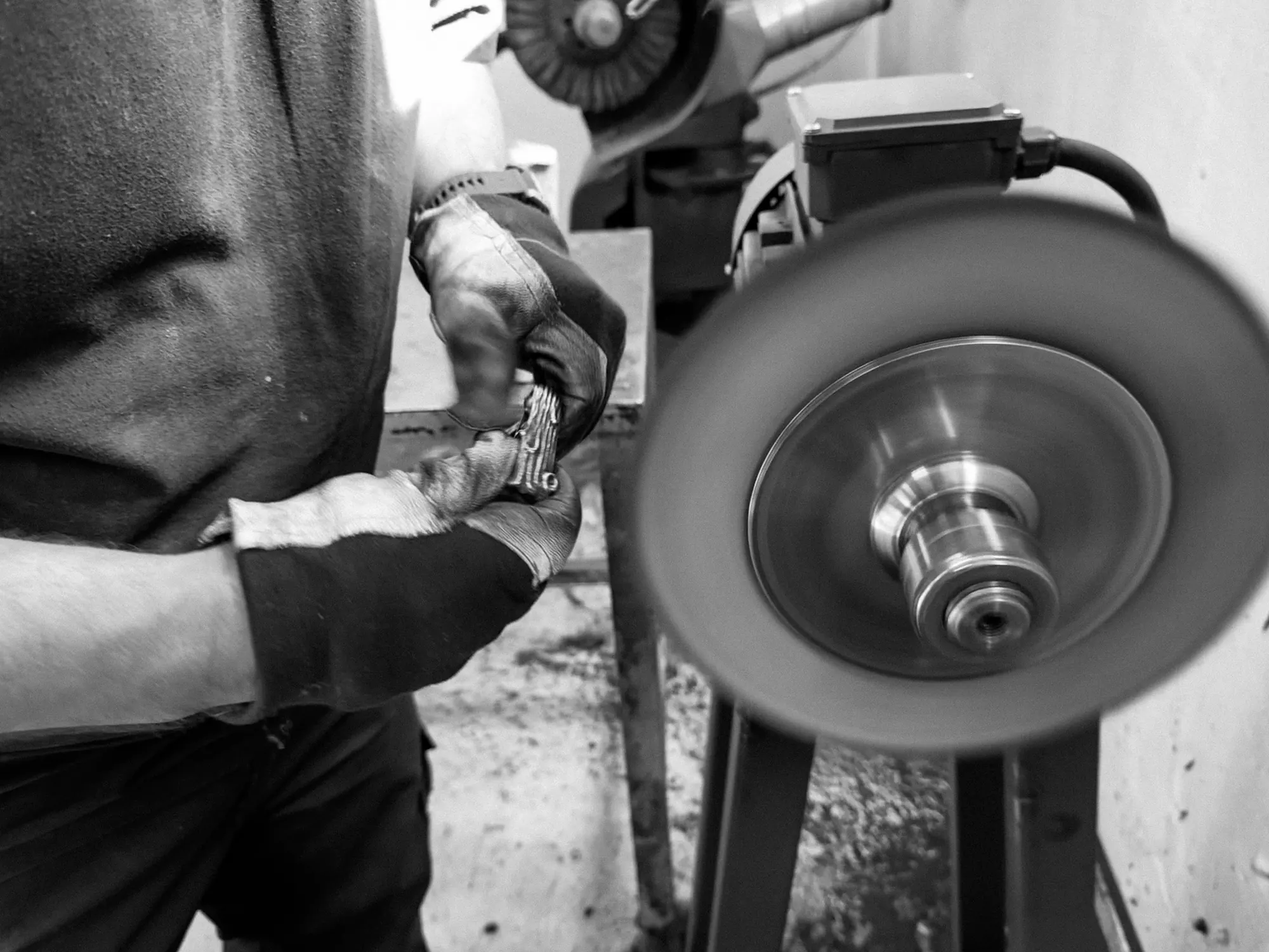 Gloved hands holding a small metal charm beside a spinning polishing wheel