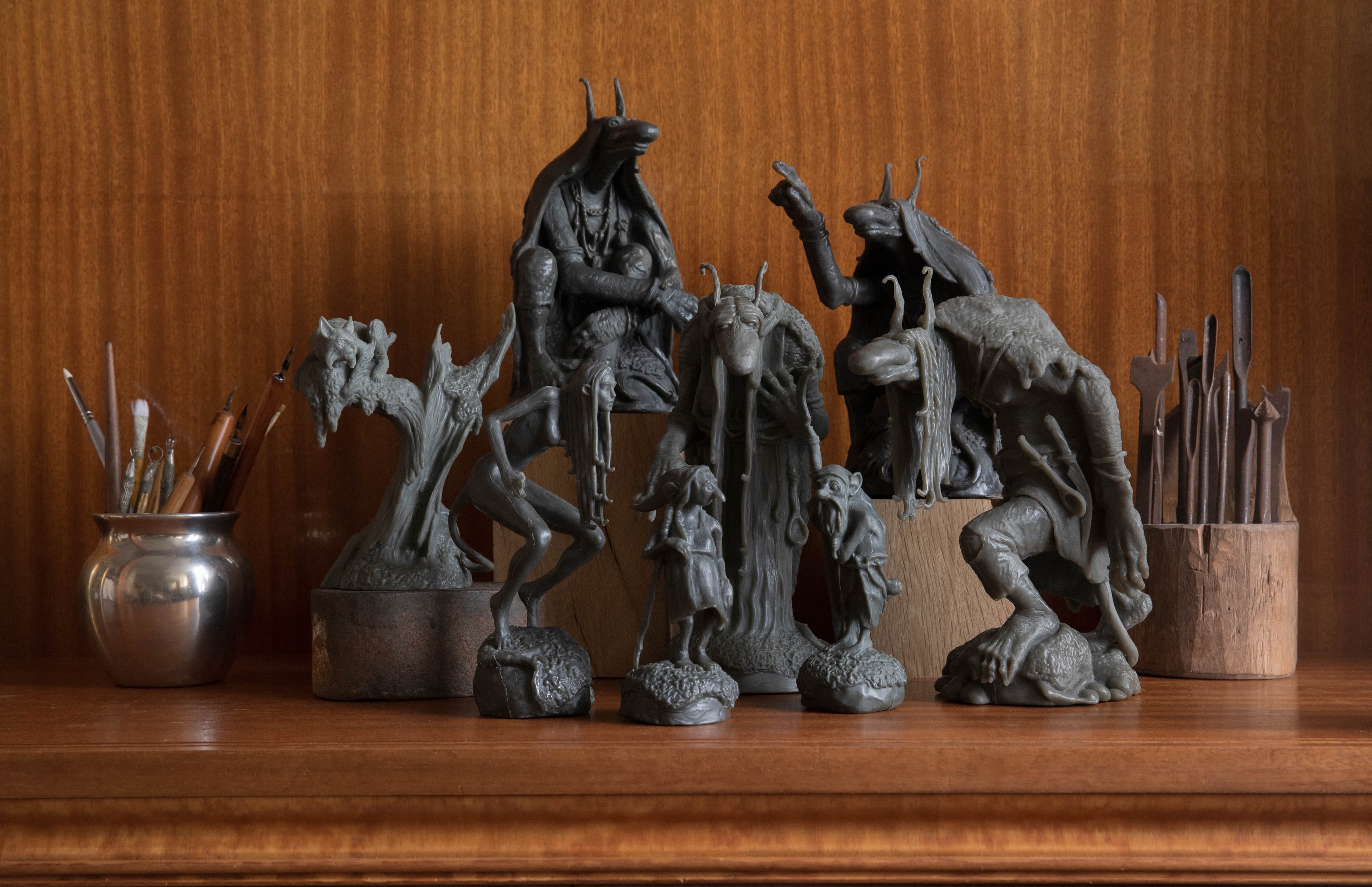 Dark Forest Green scale statues gathered on a wooden shelf beside paintbrushes and sculpting tools